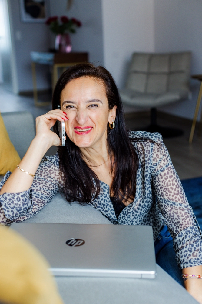 Sevtap Züberi schaut lächelnd und hat dabei einen Laptop vor sich und ein Handy am Ohr.