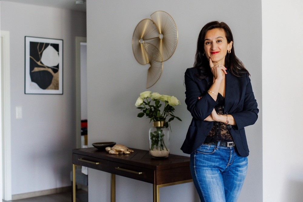 Sevtap Züberi steht vor einem schicken Holztisch, auf dem weiße Rosen stehen und lächelt.